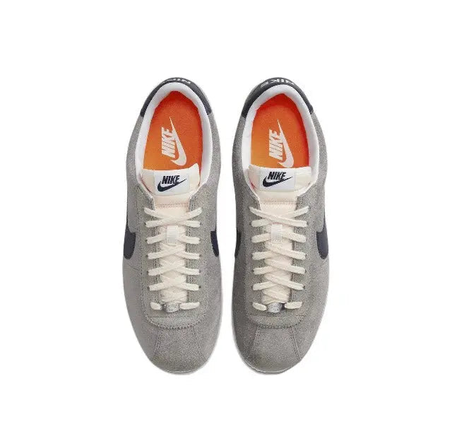 Grey Nike Cortez lace-up sneakers with orange-tinted tongue and white swoosh