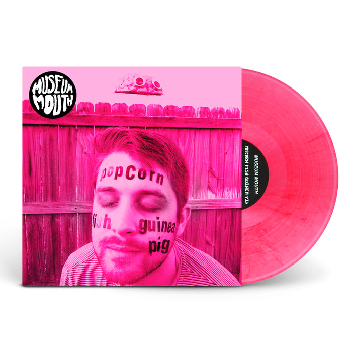 A limited edition transparent pink LP by Museum Mouth sits next to its album cover, featuring a man with “popcorn,” “fish,” and “guinea pig” on his face, a pink brain, and the Museum Mouth Popcorn Fish logo at the top.